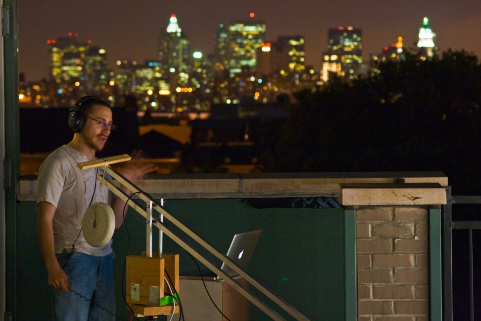 A BullsEye crew member works beside camera equipment against a nighttime city skyline.