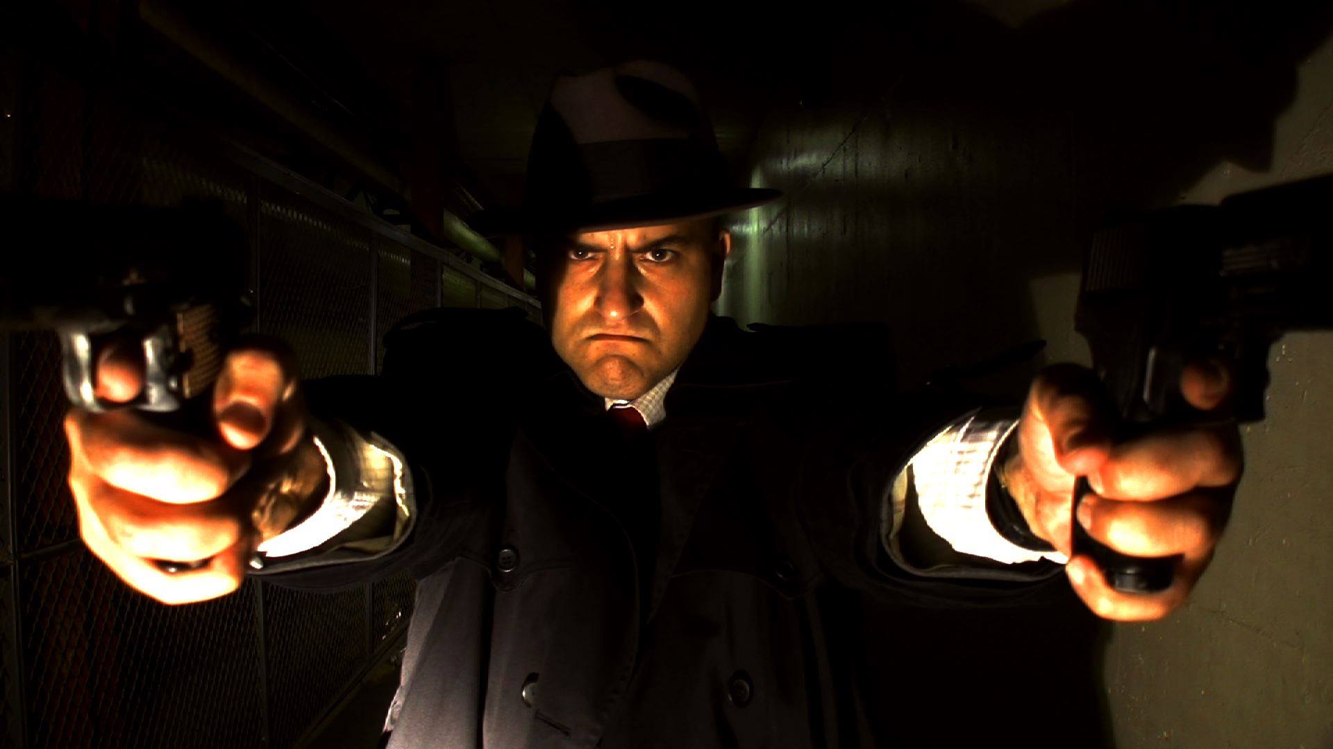 Dick Polakowski aims two prop pistols toward the camera in a dark corridor.